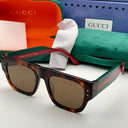 Tortoiseshell glasses with red and green accents on a white surface, Gucci branded case and box in the background.