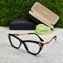 Black and gold eyeglasses with case and cleaning cloth on a textured surface with grass background