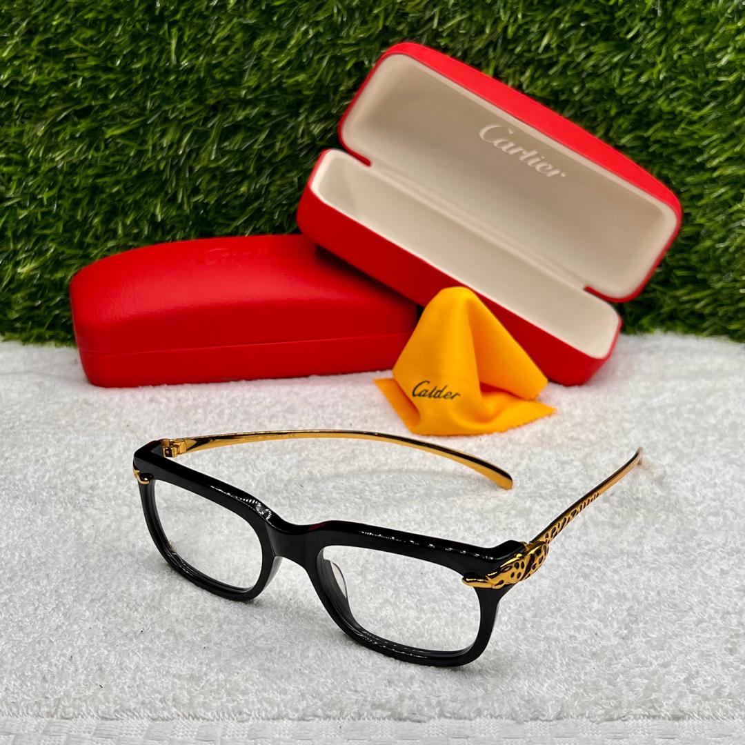 Black and gold eyeglasses with a red Cartier case on a white surface with grass background