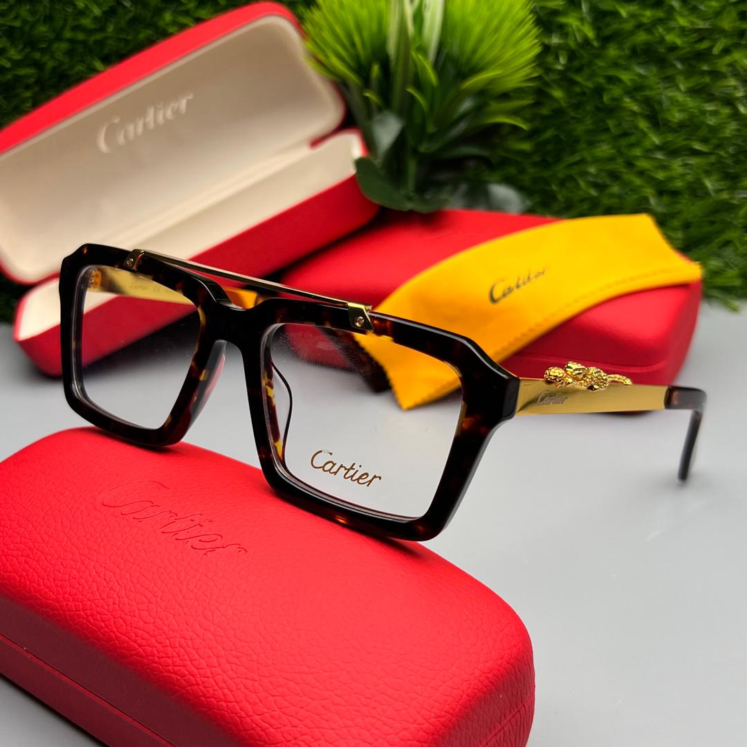 Cartier eyeglasses with gold accents on a red case with a yellow interior, against a green grass background.