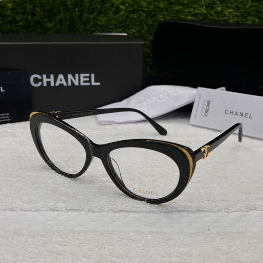 Chanel eyeglasses with black frame and gold accents on a textured surface, with Chanel branding in the background.