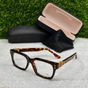 Tortoiseshell eyeglasses with gold accents on a textured surface with a grass background