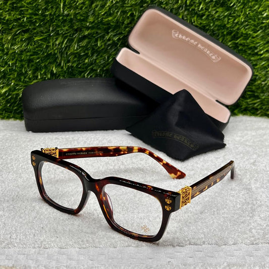 Tortoiseshell eyeglasses with gold accents on a textured surface with a grass background
