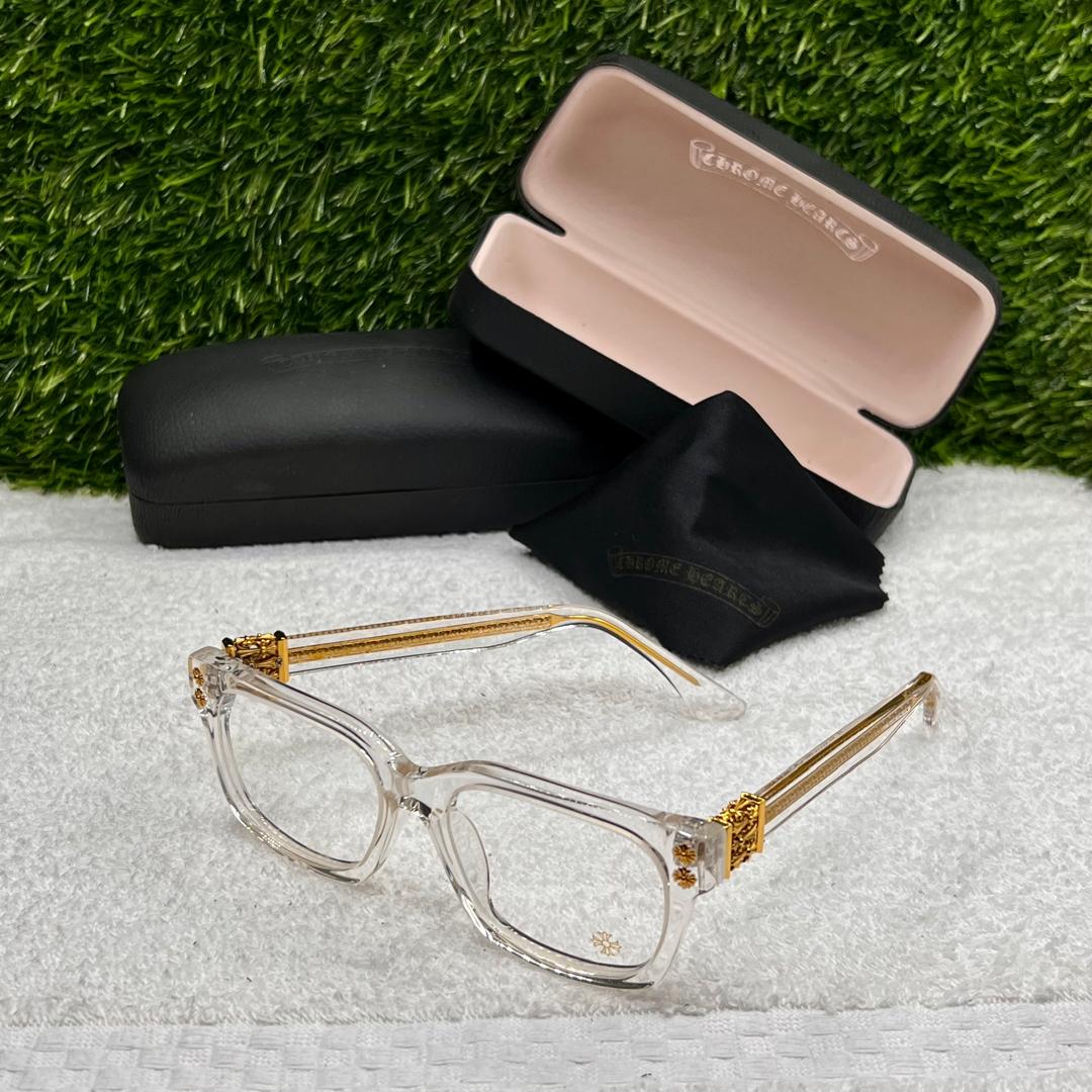 Clear/Gold-framed eyeglasses with a black case on a textured surface with grass background