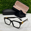 Black and gold eyeglasses with a case on a textured surface with grass background