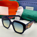 Gucci sunglasses with logo on a white surface, surrounded by Gucci packaging.