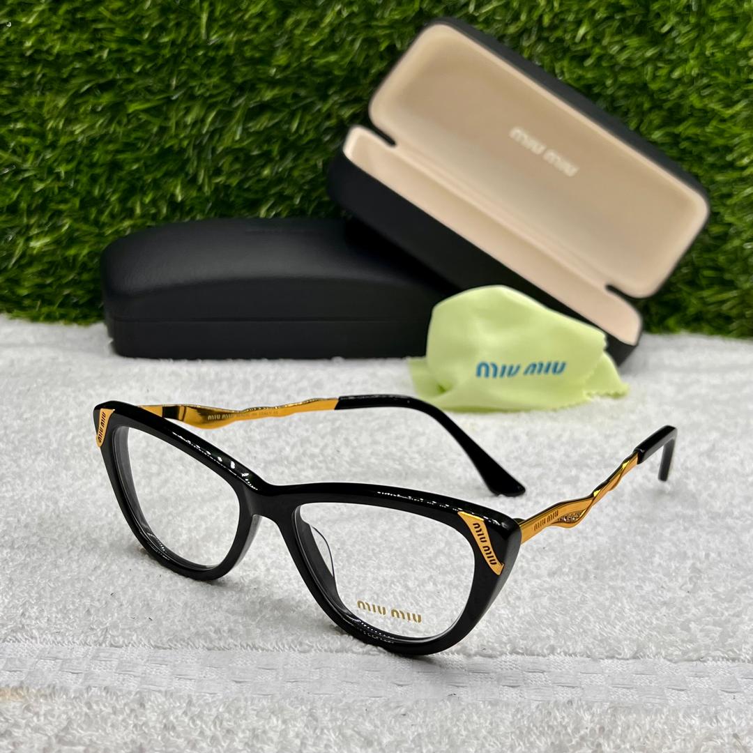 Black and gold eyeglasses with case and cleaning cloth on a textured surface with grass background