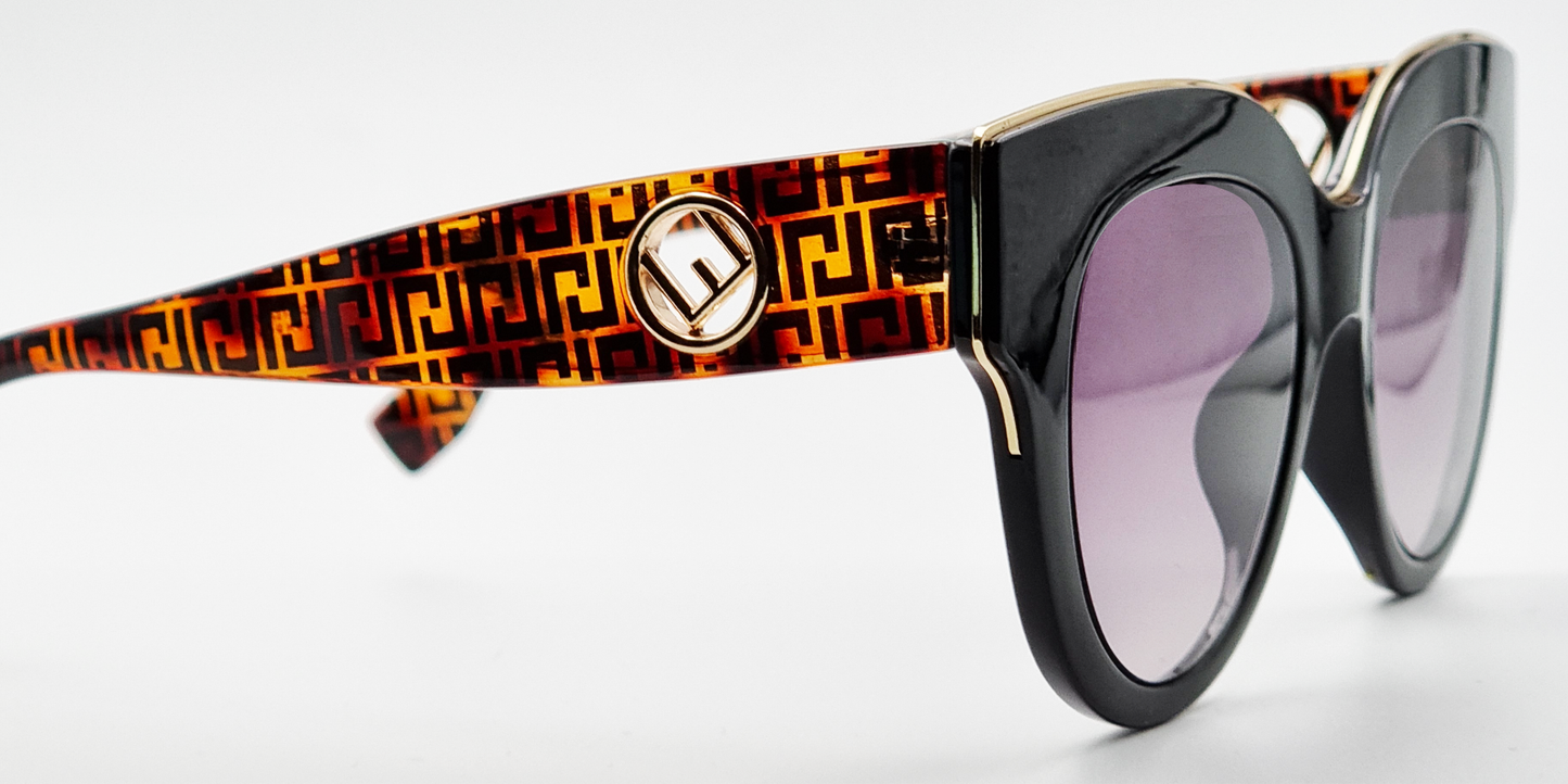 Large moulded, all-in-one, black frame glasses housing round lenses. Showing gold detail across the top of the frame and thick patterned arms with gold embellishment. side view with tinted lenses