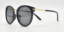 Side view. Round black frame showing tinted lenses, gold coloured bridge and gold colour on top half or ams.
