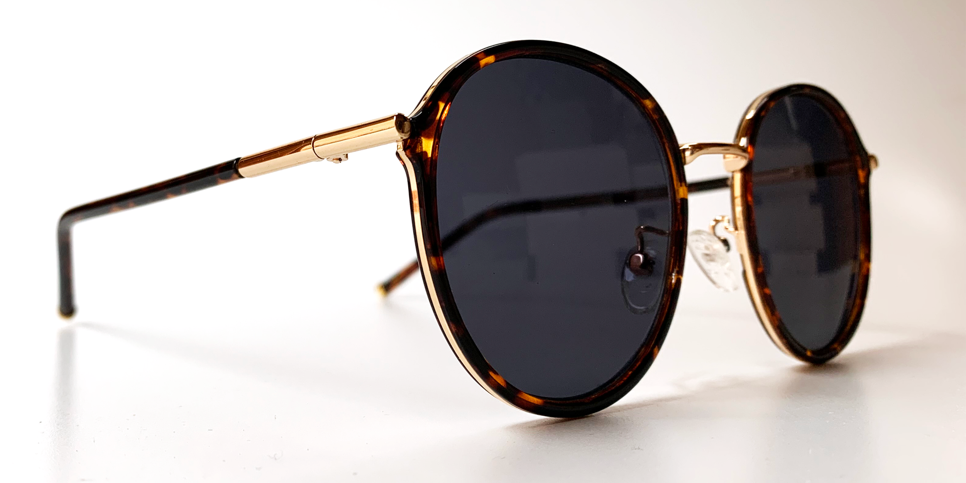 side view of round retro-style tortoiseshell frame with tinted lenses, gold coloured bridge and gold embellishments around the frame and top of the arms