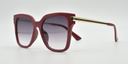 side view red rounded rectangular frame with small circular detail on front extending down the arms. Tinted lenses.