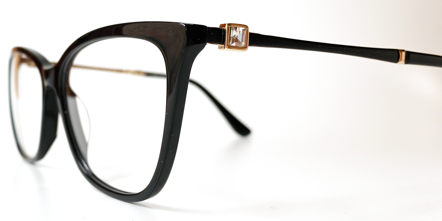 side view. showing square crystal feature, with gold coloured surround, close to the hinge area Black cat's-eye frame glasses. Gold inner, black outer coloured arms.