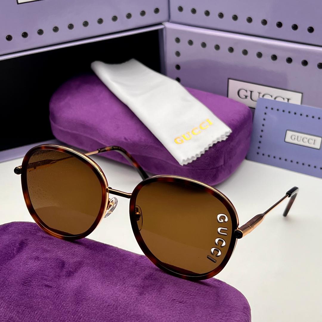 Gucci glasses with brown lenses on a purple cushion, with Gucci box and cloth in the background.